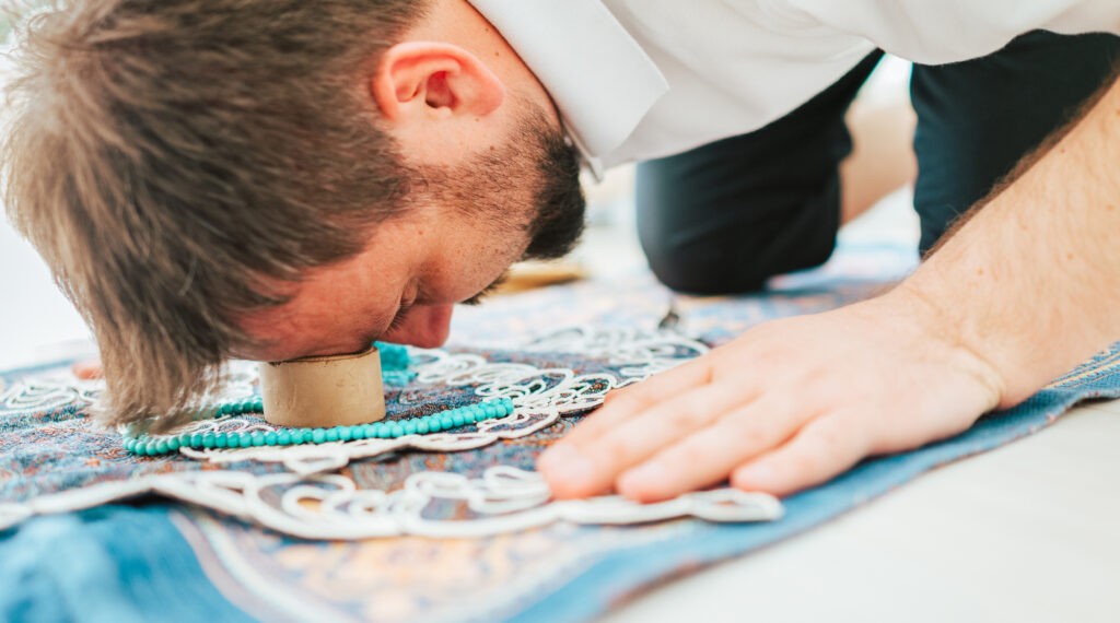  A man in prostration (sujood) on a prayer mat, with his forehead touching a turbah. 