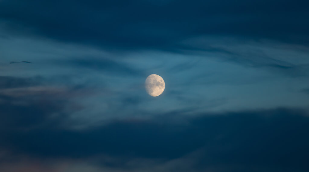 A serene image of the moon glowing softly in a cloudy evening sky, symbolizing tranquility and the peaceful ambiance of the night.