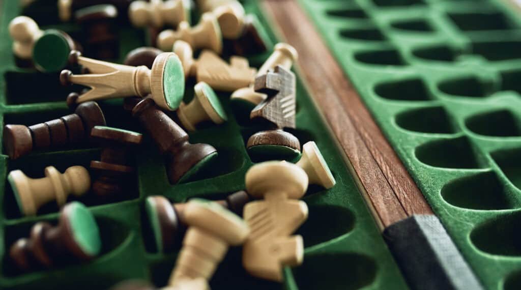 A green velvet-lined wooden chess piece storage box with scattered wooden chess pieces, some facing down, showing green felt bases. The box highlights its storage functionality.