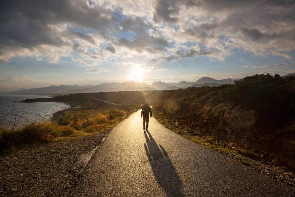 Scenic road in the mountains. Travel background. Man going on sunrise background.