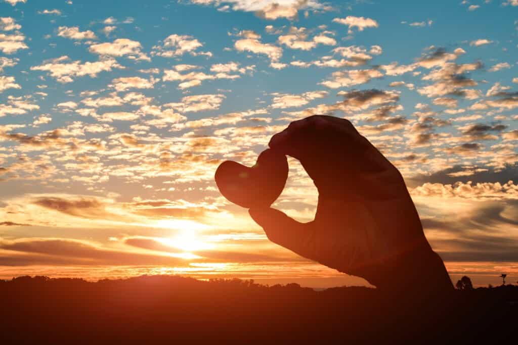 Silhouette of hands holding hearts on sunset sky background