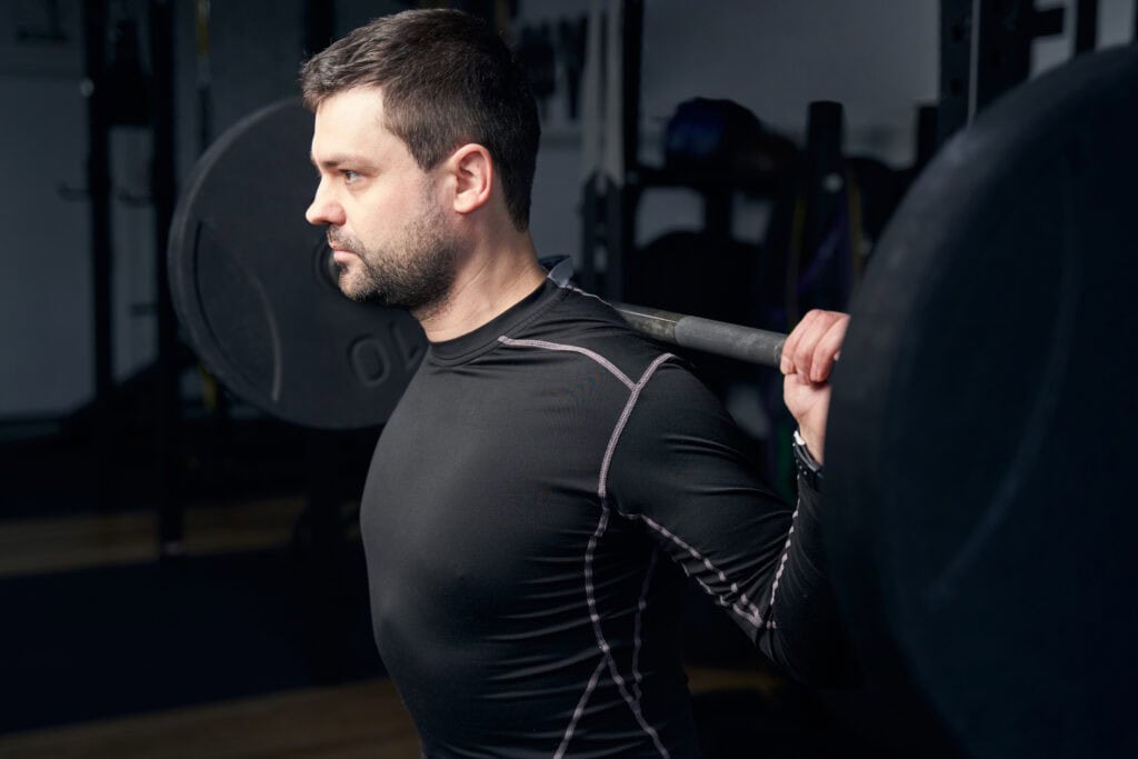 Bearded male athlete lifting heavy weight using gym exercise equipment while having workout in sport club